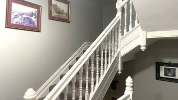 Una escalera con balaustres blancos y barandilla, que sube a un piso superior.