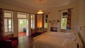 A bedroom with two beds, a red chair, a table with chairs, and a window with curtains.