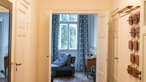 Een hal met een kamerbreed tapijt, een moderne lamp en uitzicht op een kamer met een bank en gordijnen.