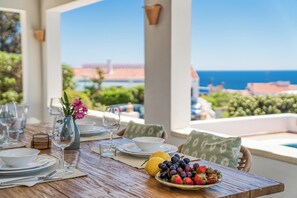Ein Tisch, gedeckt für eine Mahlzeit, mit Blick auf das Meer, einer Obstschale und einem Blumenstrauß.