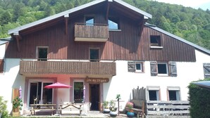 Un immeuble de deux étages doté d’un balcon, d’une enseigne indiquant « Cite des S+pins », et d’un espace extérieur aménagé avec des tables et des parasols.