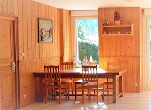 Enjoy meals in this cozy dining area with a wooden table and chairs, surrounded by a view of lush greenery.