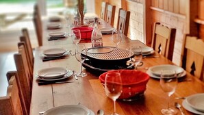 Une table de salle à manger en bois, mise avec des assiettes, des couverts, des verres et un barbecue portable.