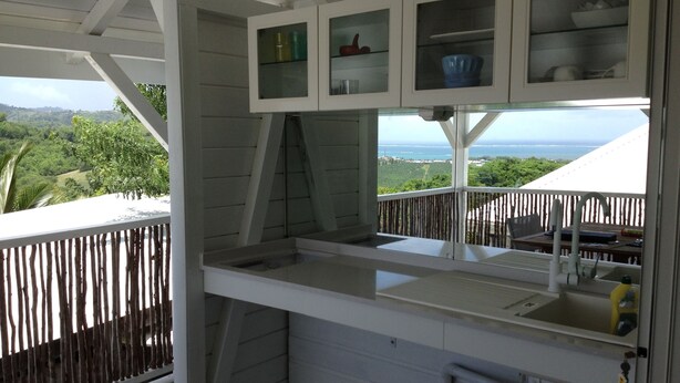 A kitchen with a view of the ocean, a wooden deck, and a white exterior. - Beautiful new bungalow with views. (Le vauclin)