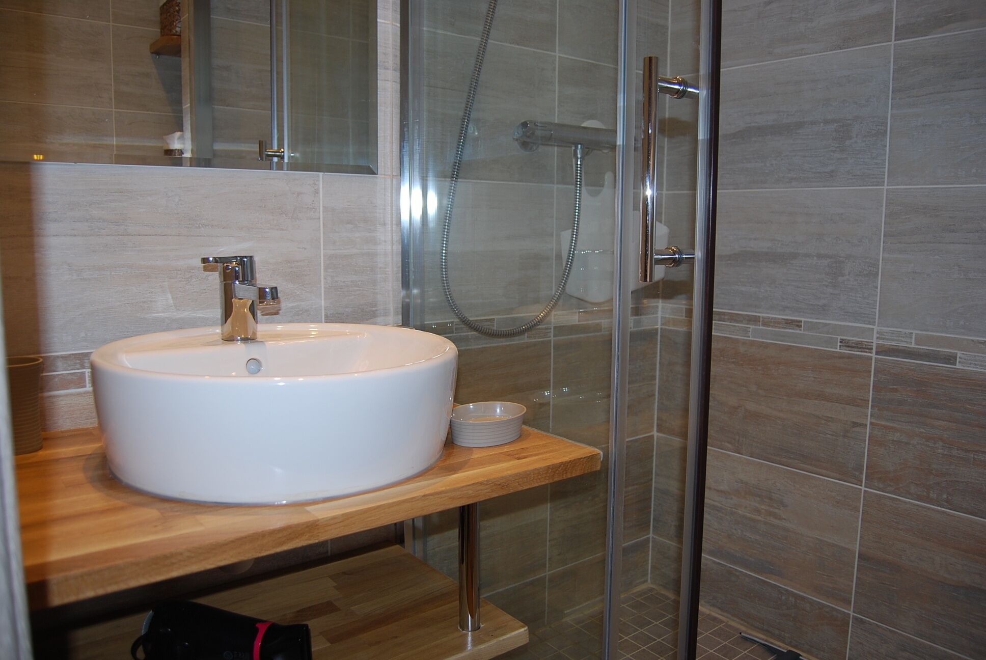 Ein modernes Badezimmer mit einem weißen Waschbecken, einer Duschkabine aus Glas und einem hölzernen Waschtisch.