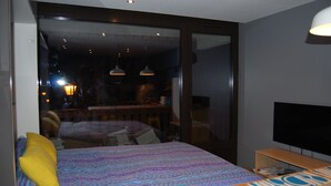 Une chambre avec un lit, un bureau, une télévision et un balcon offrant une vue sur la ville la nuit.
