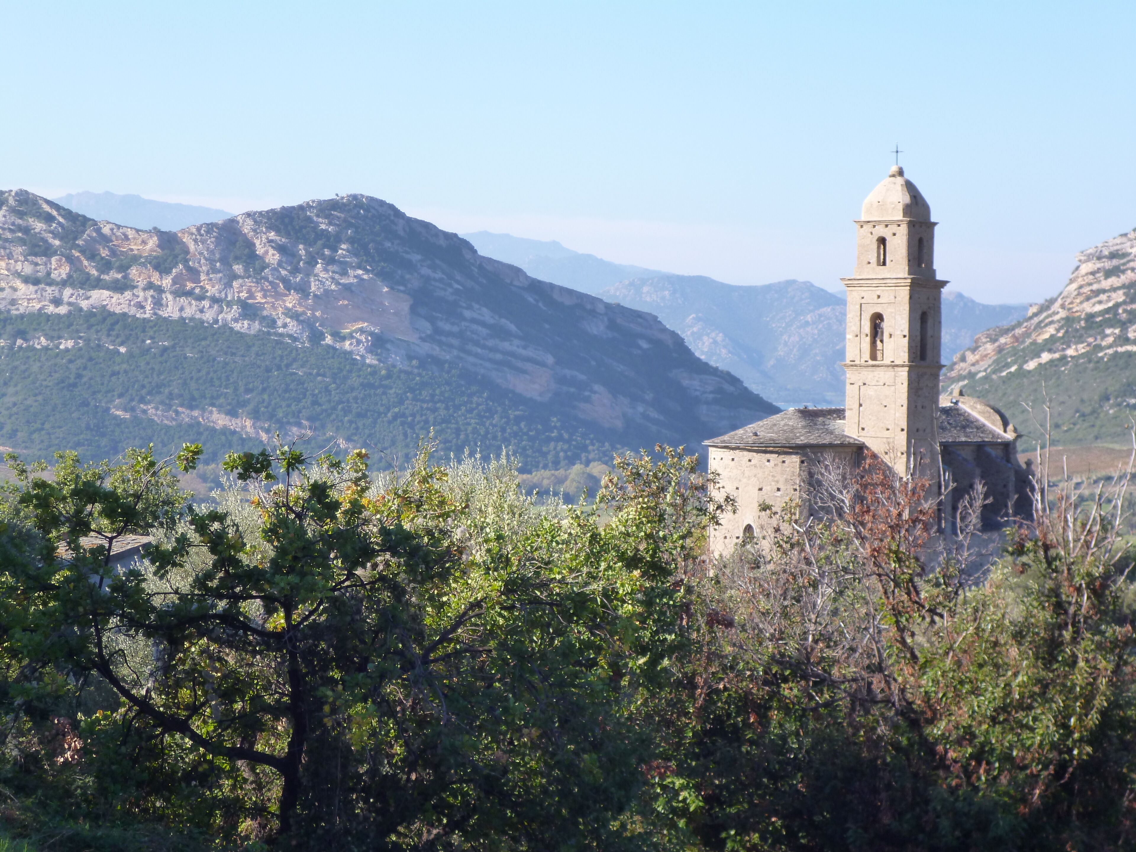 A church with a bell tower surrounded by mountainous terrain and dense foliage.