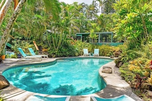 A swimming pool surrounded by lush greenery, with lounge chairs and a building in the background.