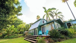 A house with a deck, surrounded by lush greenery and palm trees. - Private Hot Tub + Pool Access + AC - Star Lookout (Haiku)