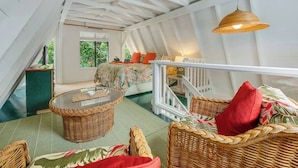A room with a high ceiling, a bed with floral bedding, wicker furniture, and a view of greenery outside. - Private Hot Tub + Pool Access + AC - Star Lookout (Haiku)