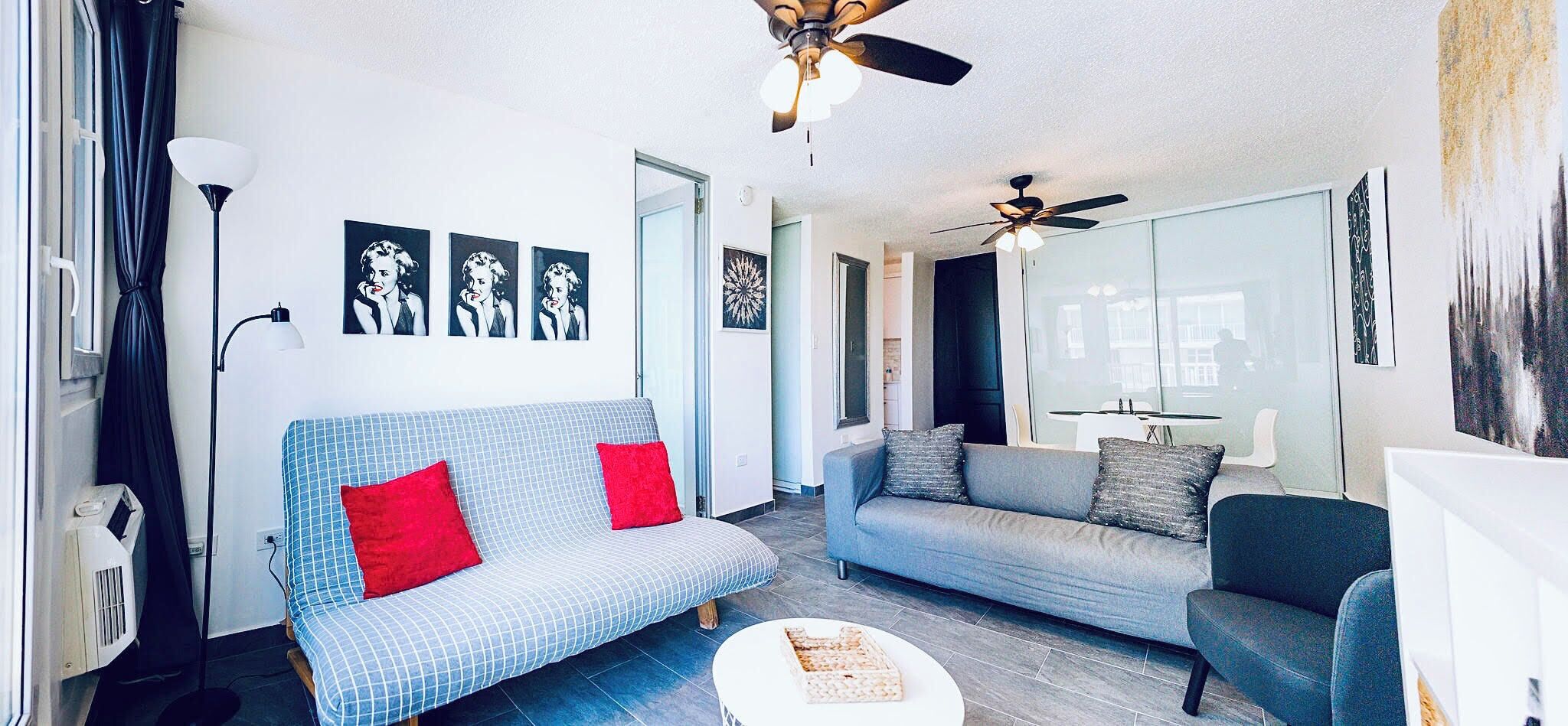 A modern living room with two sofas, a coffee table, and ceiling fans.