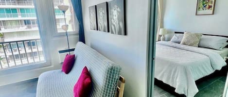 Ein modernes Hotelzimmer mit einem großen Bett, einem kleinen Sofa und einem Balkon mit Blick auf die Stadt.