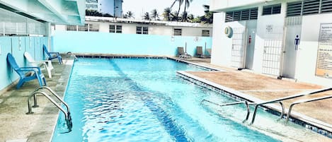 Una piscina con agua azul, rodeada de sillas de descanso y un edificio con un letrero que dice 'WBC HOTEL'.