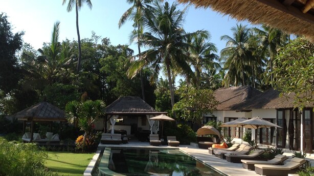 A poolside area with lounge chairs, a thatched-roof structure, and palm trees. - Large luxury beach villa, max 10 people, beautiful volume, typical Balinese (kubutambahan)