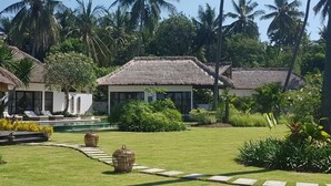 A resort with thatched-roof cottages, a well-maintained lawn, and palm trees. - Large luxury beach villa, max 10 people, beautiful volume, typical Balinese (kubutambahan)