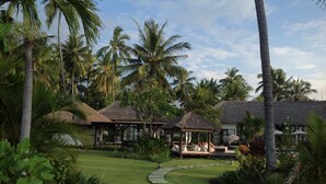 A tropical resort with thatched-roof huts, a well-maintained lawn, and palm trees. - Large luxury beach villa, max 10 people, beautiful volume, typical Balinese (kubutambahan)