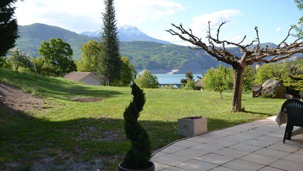 A garden area with a potted tree, a bench, and a view of a lake and mountains in the background.