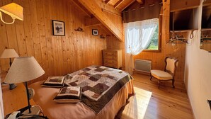 A wooden cabin bedroom with a bed, bedside lamps, a dresser, a chair, and a window with curtains.