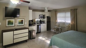 A compact hotel room with a kitchenette, a bed, a desk, and a ceiling fan. - King One Bedroom Overlooking the Pool (Naples)