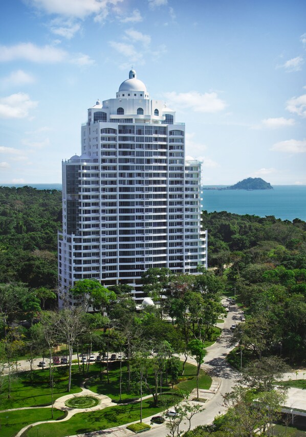 Un hôtel de grande hauteur, surmonté d’un dôme central, entouré d’une végétation luxuriante et offrant une vue sur la mer.