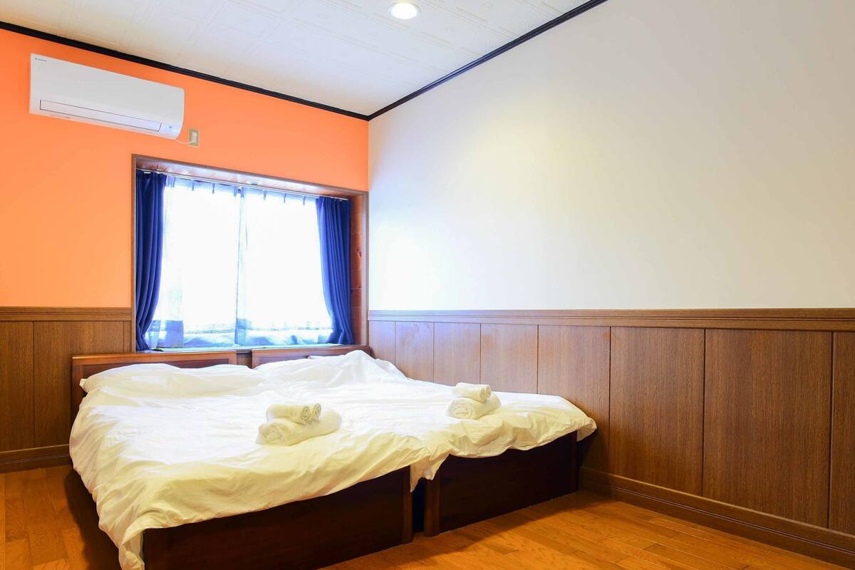 Habitación de hotel con cama de madera, ventana con cortinas y un equipo de aire acondicionado en la pared.