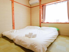 A room with a bed, a window with curtains, and an air conditioning unit. - Vacation House Familia (Kozushima-mura)
