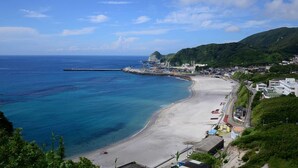 Un pueblo costero con playa, un muelle y montañas al fondo.
