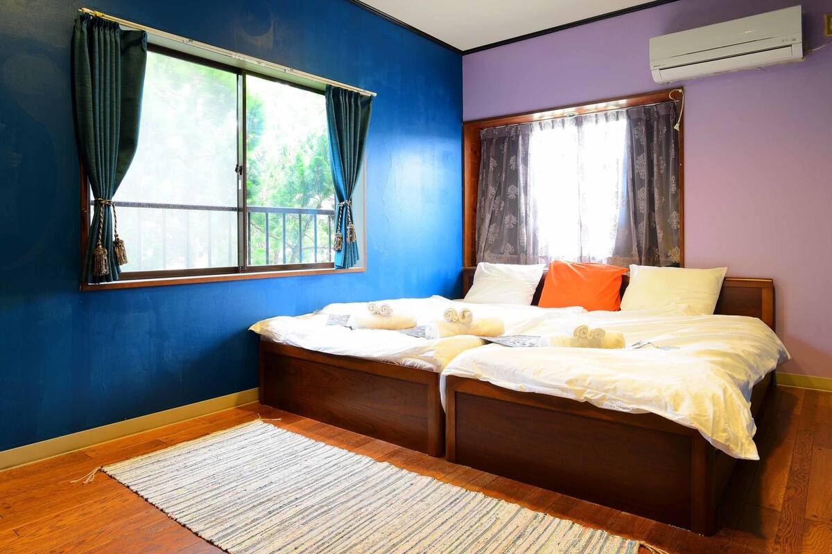 Un dormitorio con una cama grande, dos ventanas con cortinas, aire acondicionado y suelo de madera.