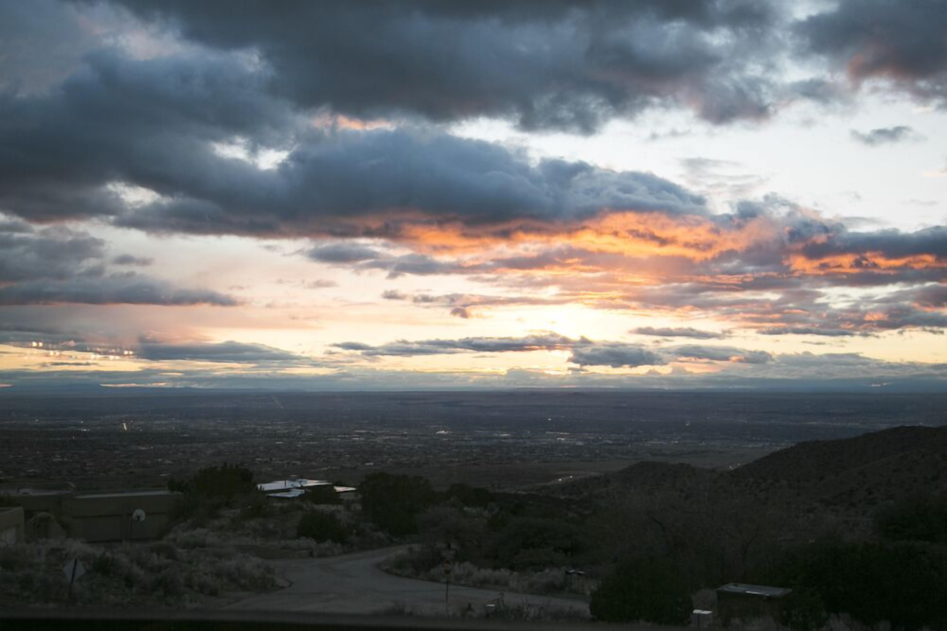 A panoramic view of a cityscape with a sunset over the horizon, featuring a mix of urban and natural landscapes.