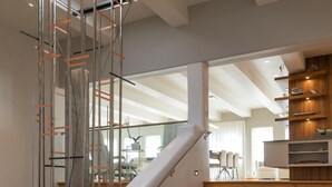 A modern staircase with wooden steps and a metal handrail, leading to a bright room with a dining area and kitchen in the background.