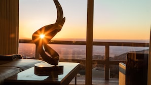 A room with a large window, a sculpture on a table, and a view of a cityscape at sunset.