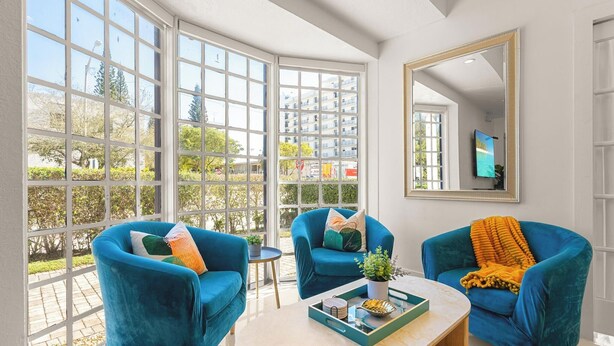 A modern living room with large windows, two blue armchairs, a coffee table with decorative items, and a mirror on the wall. - Villa Diamond in South Beach (Miami Beach)