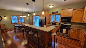 A kitchen with wooden cabinets, a stainless steel refrigerator, a stove, and a bar area with stools. - Beautiful Pristine O'brien Lake Home in Crosslake MN, Sleeps 10 (Crosslake)