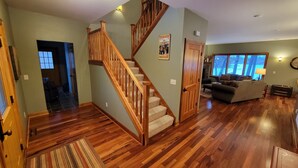 A spacious living area with a wooden staircase, a fireplace, and a large window providing a view of the outdoors. - Beautiful Pristine O'brien Lake Home in Crosslake MN, Sleeps 10 (Crosslake)
