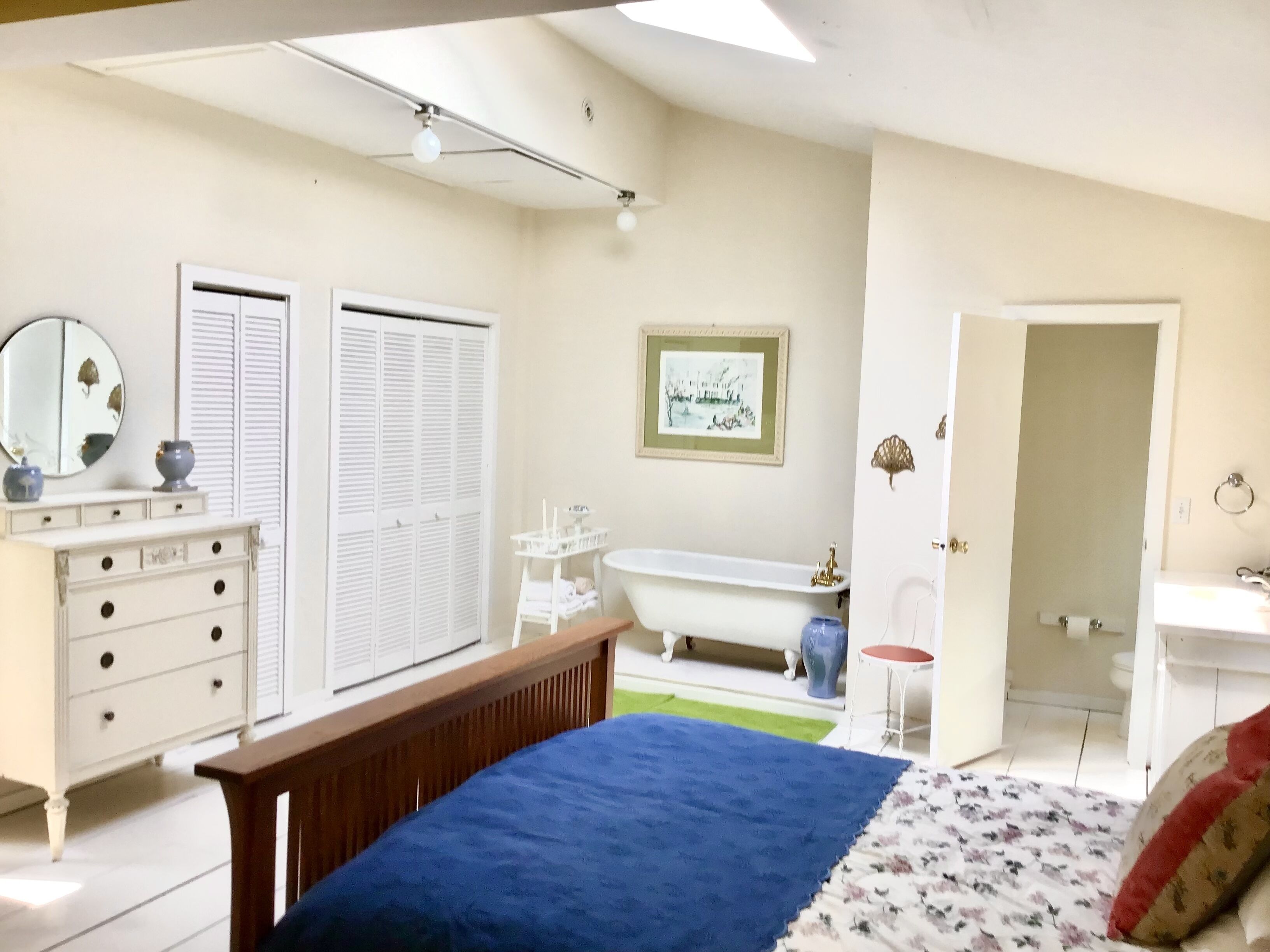Een slaapkamer met een bed, een dressoir, een kaptafel, een badkuip en een deur naar een andere kamer.