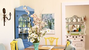 Uma sala de jantar com uma mesa de madeira, cadeiras amarelas, uma porta azul e um armário branco decorado.