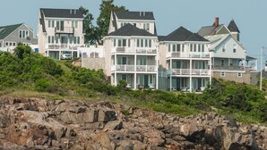 A coastal residential area with multi-story houses featuring balconies and large windows, situated on a rocky shoreline with a view of the sea. - Exclusive Oceanfront Retreat with Endless Atlantic Views (York Beach)