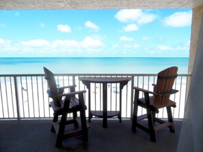 Un balcon avec deux fauteuils Adirondack et une petite table, offrant une vue dégagée sur la plage et l’océan.