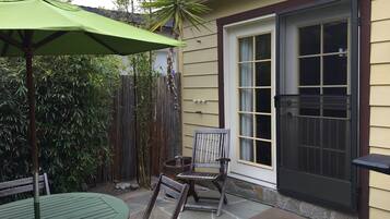 Une terrasse avec un parasol vert, une table en pierre et deux chaises en bois.