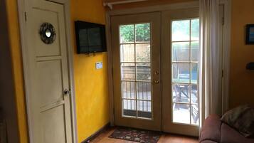 Una habitación con una pared amarilla, una puerta blanca, un vidrio corredero, un televisor montado en la pared y un sofá marrón.
