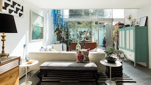 Een moderne woonkamer met een bank, een lange zitbank, een salontafel en een kast. Er is een raam met uitzicht op groen buiten.