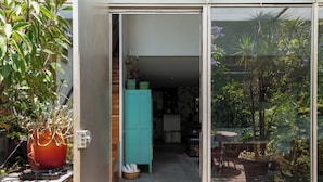 Een modern huis met een glazen deur die uitkomt op een patio met potplanten en een blauwgroene kast.