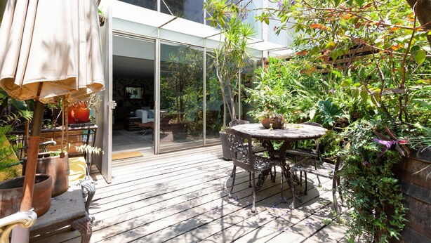 Een terras buiten met een houten terras, een ronde tafel en stoelen.