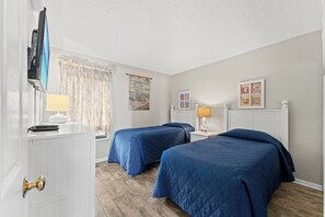 Ein Hotelzimmer mit zwei Betten, einem Schreibtisch mit Computer, einer Lampe und Bildern an den Wänden.
