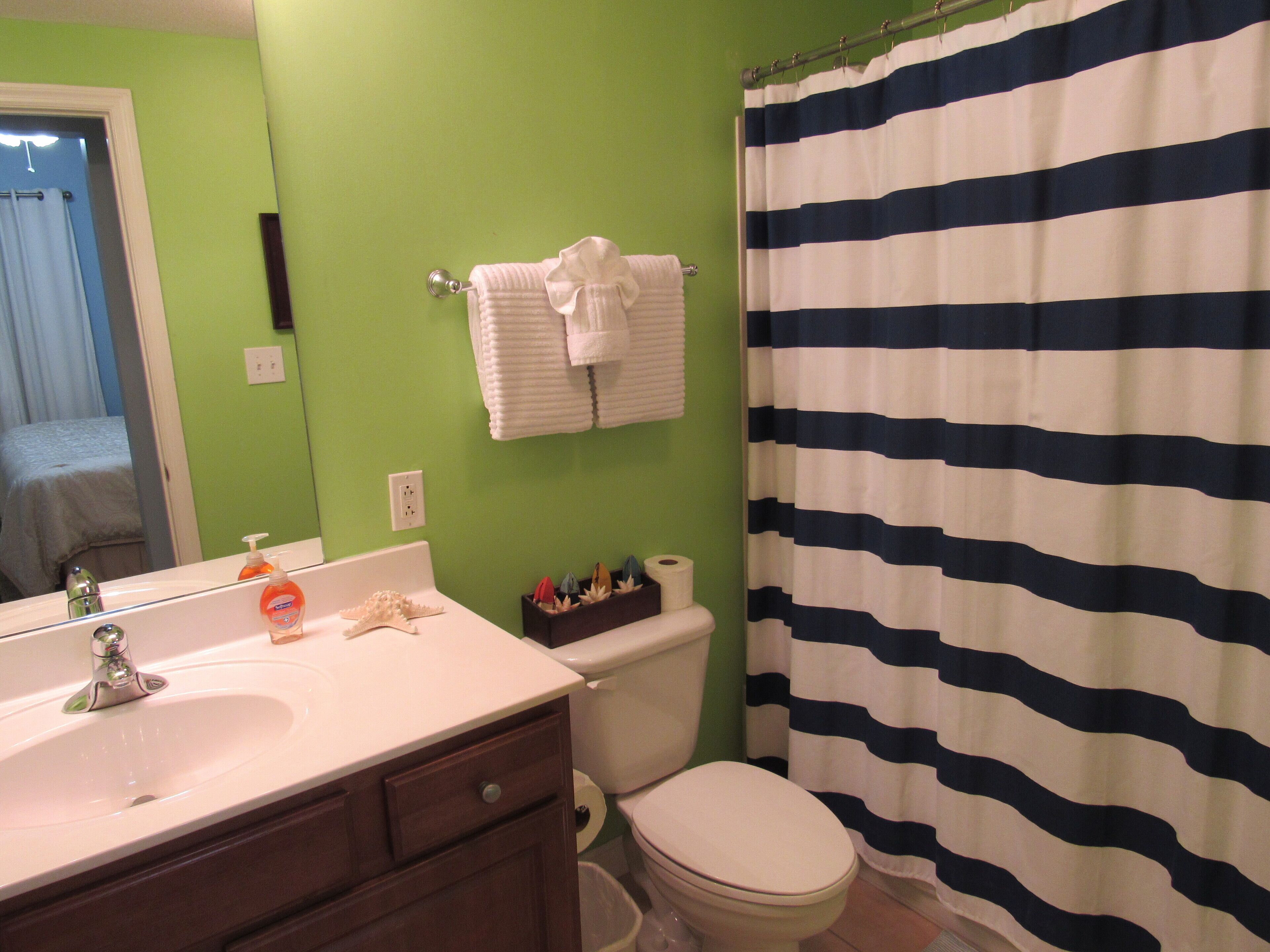 A bathroom with a green wall, a white sink, a white toilet, and a striped shower curtain.