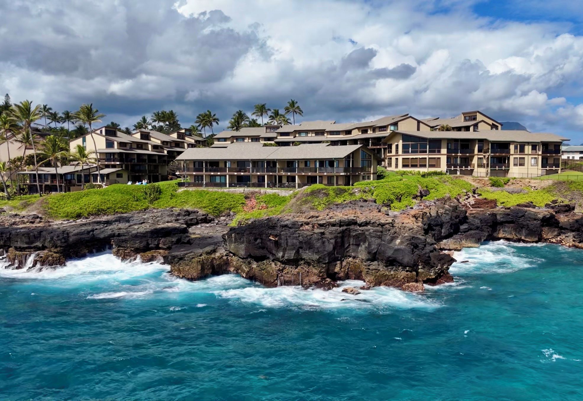 A coastal hotel with multiple buildings, a rocky shoreline, and ocean waves.