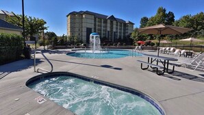 Zona de piscina de hotel con jacuzzi, sillas de descanso y una fuente de agua.