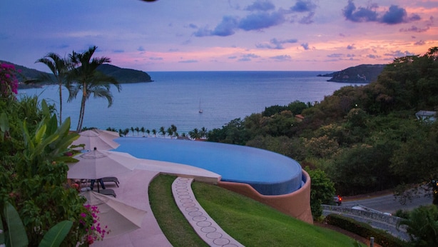 A resort with a swimming pool, palm trees, and a view of the sea at sunset. - The Beach is Calling!  Book November & December NOW! (Zihuatanejo)