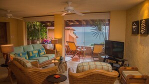 A living room with wicker furniture, a television, and a view of the ocean. - The Beach is Calling!  Book November & December NOW! (Zihuatanejo)