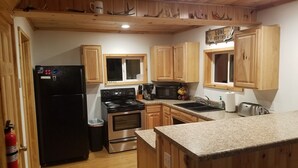 A kitchen with wooden cabinets, a black refrigerator, a stove, a microwave, and a sink. - Petoskey - Enjoy the great outdoors from the Cozy and peaceful cabin! (Petoskey)